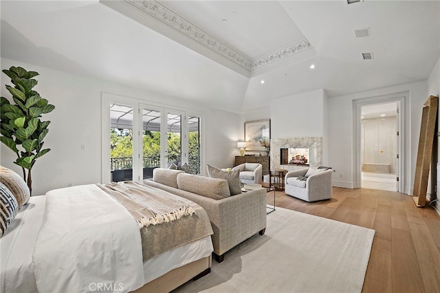 bedroom with ensuite bath, access to exterior, french doors, light hardwood / wood-style flooring, and a raised ceiling