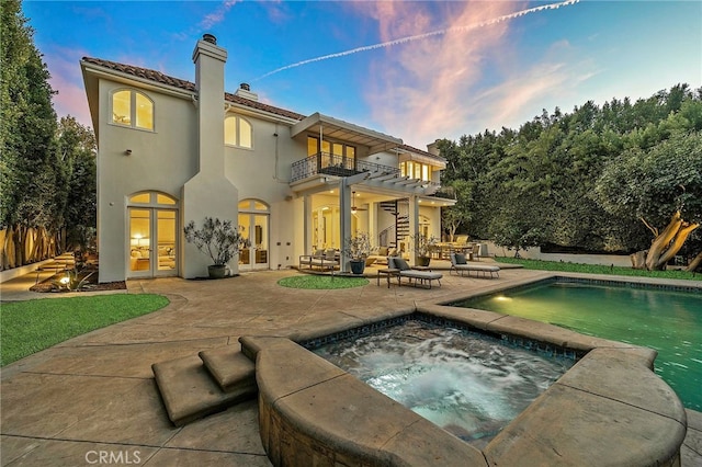 back house at dusk featuring a balcony, a swimming pool with hot tub, and a patio area