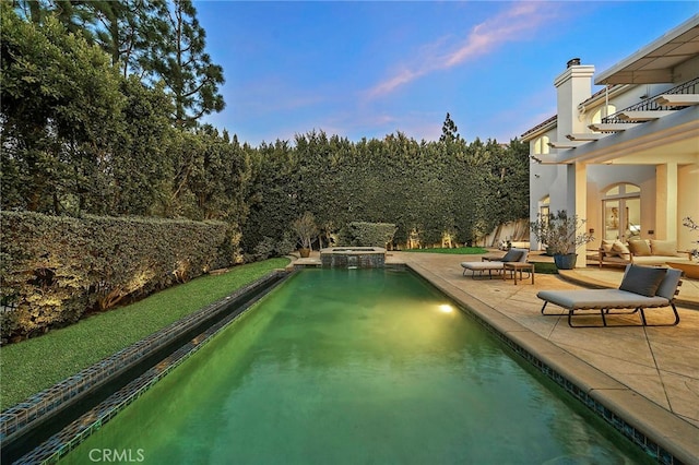 pool at dusk featuring an outdoor hangout area, a patio, and an in ground hot tub