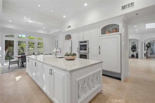 kitchen featuring light tile flooring, white cabinets, light stone counters, a kitchen island with sink, and sink