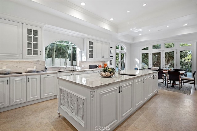 kitchen featuring light stone countertops, white cabinetry, backsplash, and an island with sink