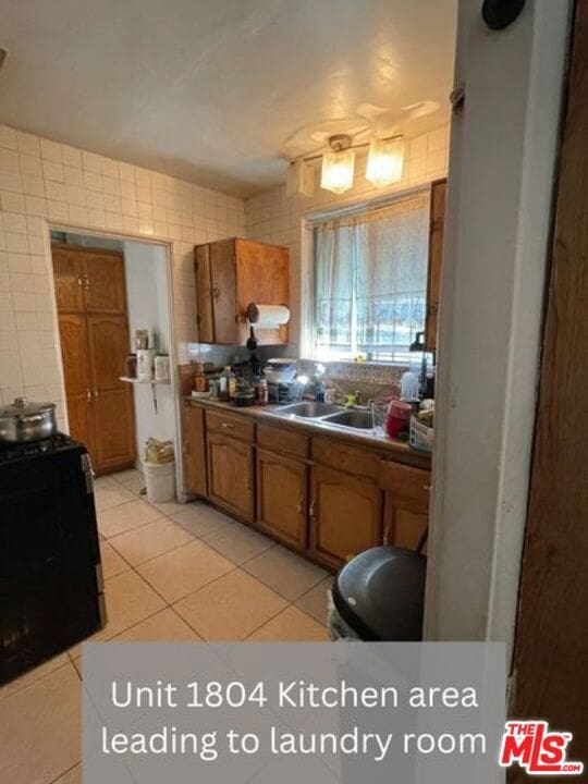 kitchen featuring stove, sink, light tile flooring, and tile walls