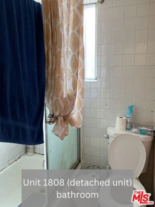 bathroom featuring toilet, tile walls, and a wealth of natural light