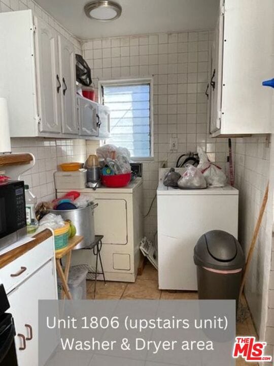 clothes washing area with tile walls, cabinets, independent washer and dryer, and light tile floors