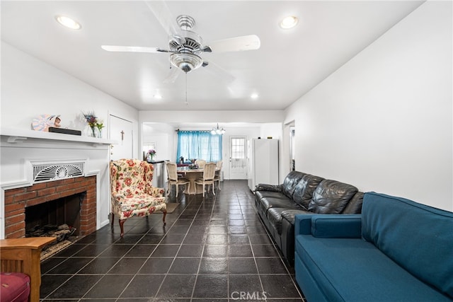 living room with a fireplace, ceiling fan with notable chandelier, and dark tile flooring