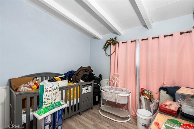 bedroom with beam ceiling, a nursery area, and light hardwood / wood-style floors