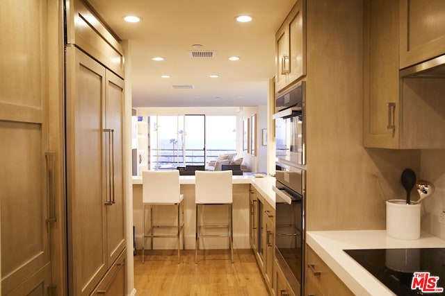 kitchen featuring multiple ovens, light hardwood / wood-style floors, and black electric cooktop