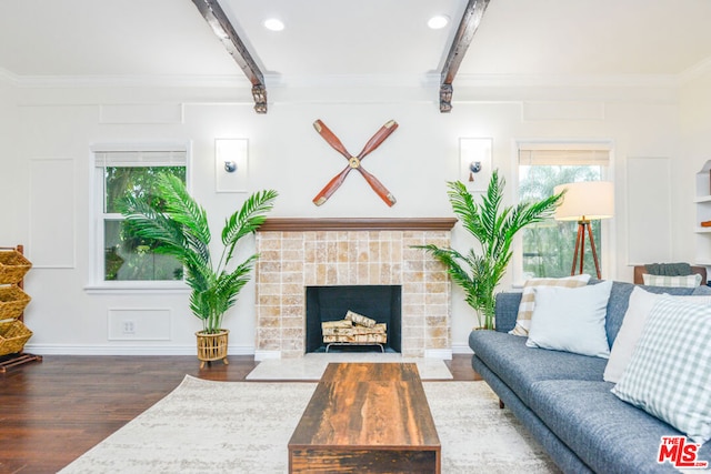 living room featuring a tiled fireplace, dark hardwood / wood-style flooring, ornamental molding, and beamed ceiling