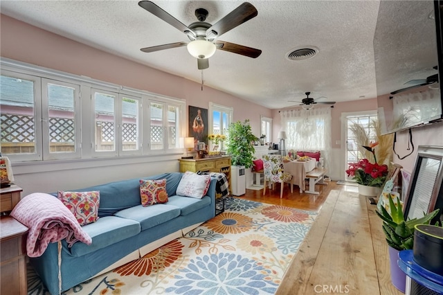 living room with ceiling fan, light hardwood / wood-style flooring, and a textured ceiling