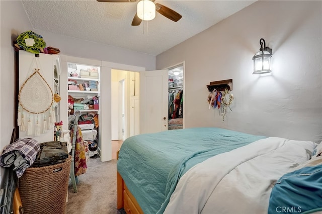 bedroom with a walk in closet, ceiling fan, light carpet, a textured ceiling, and a closet