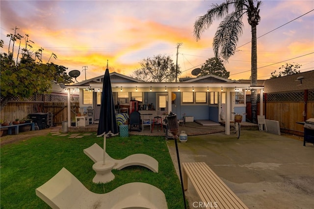 back house at dusk featuring a lawn and a patio area