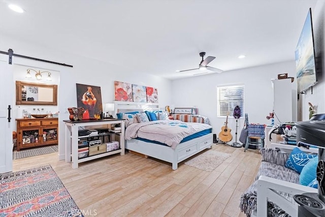 bedroom featuring ceiling fan, a barn door, and light wood-type flooring