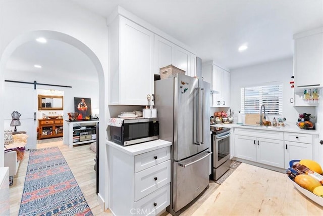 kitchen featuring sink, white cabinets, light hardwood / wood-style floors, stainless steel appliances, and a barn door