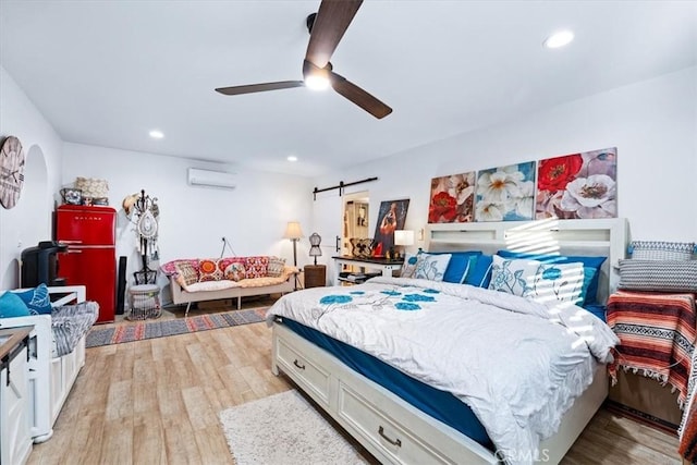 bedroom featuring ceiling fan, a barn door, a wall unit AC, and light hardwood / wood-style flooring