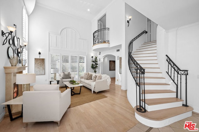 living room with a high ceiling, crown molding, and light hardwood / wood-style flooring