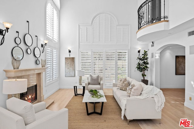 living room featuring a high ceiling, a high end fireplace, light hardwood / wood-style floors, and a healthy amount of sunlight