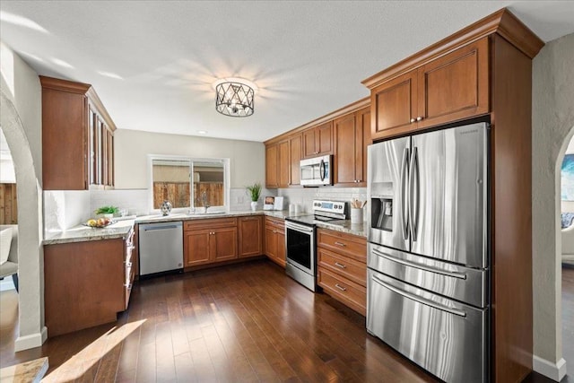 kitchen featuring backsplash, stainless steel appliances, dark hardwood / wood-style flooring, and light stone counters