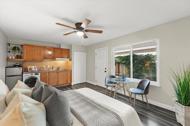 bedroom featuring dark hardwood / wood-style flooring, stainless steel refrigerator, washer / dryer, ceiling fan, and sink