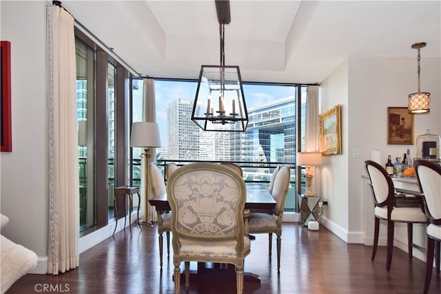 dining area with dark hardwood / wood-style floors, an inviting chandelier, a wall of windows, and a tray ceiling