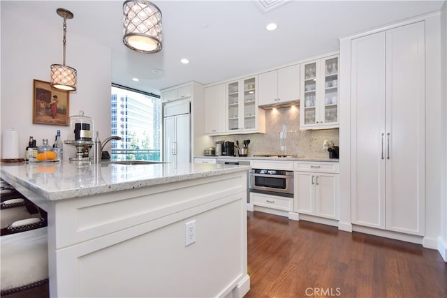 kitchen featuring decorative light fixtures, white cabinets, stainless steel oven, paneled refrigerator, and light stone countertops