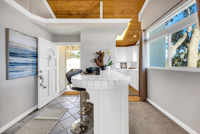 kitchen with white cabinets, a kitchen bar, tile countertops, light tile patterned flooring, and wooden ceiling