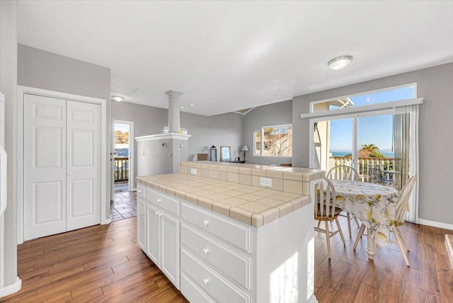 kitchen with tile countertops, a kitchen island, hardwood / wood-style floors, and white cabinetry