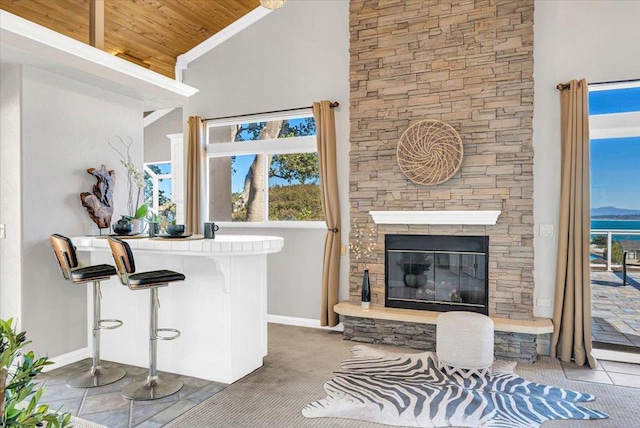 bar featuring light tile patterned floors, wooden ceiling, a stone fireplace, and high vaulted ceiling