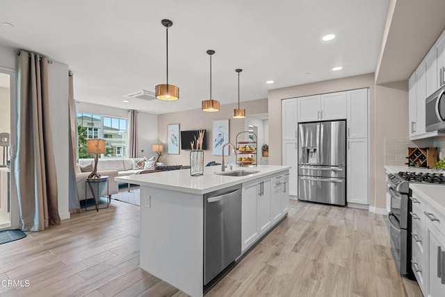 kitchen with light hardwood / wood-style floors, stainless steel appliances, decorative light fixtures, a center island with sink, and sink