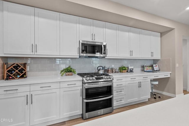 kitchen with appliances with stainless steel finishes, white cabinetry, backsplash, and light hardwood / wood-style flooring