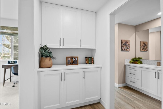 bar featuring light hardwood / wood-style flooring, sink, and white cabinetry
