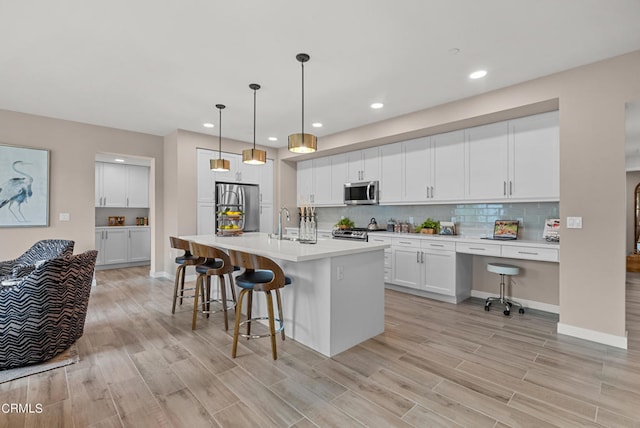 kitchen featuring a kitchen island with sink, hanging light fixtures, a breakfast bar area, stainless steel appliances, and white cabinetry
