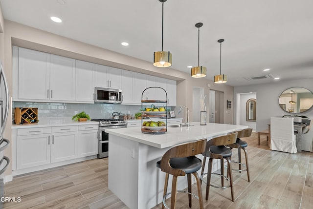 kitchen with white cabinetry, a center island with sink, stainless steel appliances, pendant lighting, and backsplash