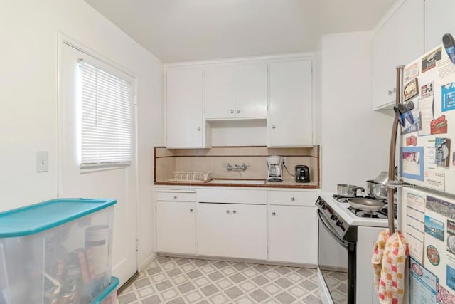 kitchen featuring stainless steel fridge, white cabinets, light tile flooring, and electric range