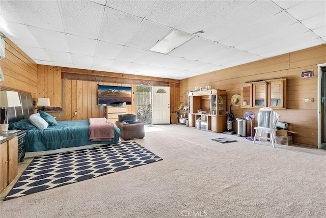 bedroom featuring light carpet, wooden walls, and a drop ceiling