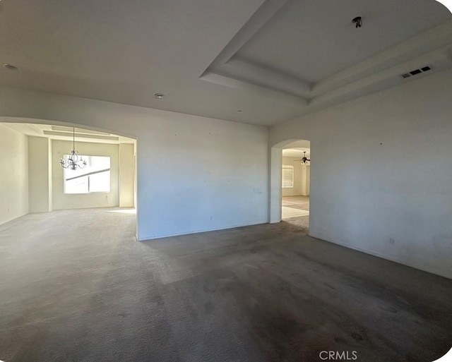 carpeted spare room featuring a tray ceiling and a notable chandelier