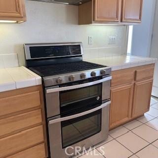 kitchen featuring tile countertops, light tile patterned flooring, and stainless steel stove