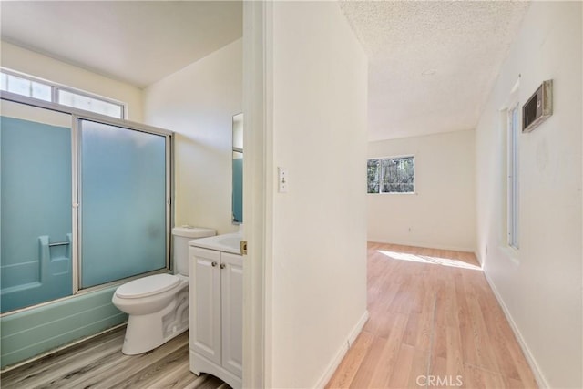bathroom featuring toilet, vanity, wood finished floors, and shower / bath combination with glass door