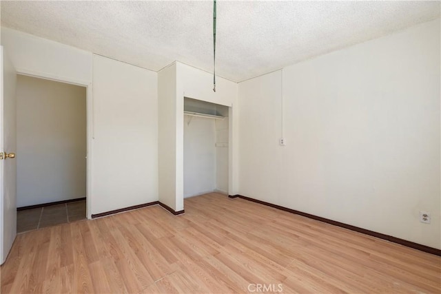 unfurnished bedroom featuring a textured ceiling, a closet, light wood finished floors, and baseboards