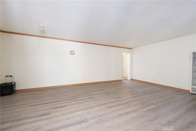 spare room with baseboards, crown molding, light wood-style floors, and a textured ceiling