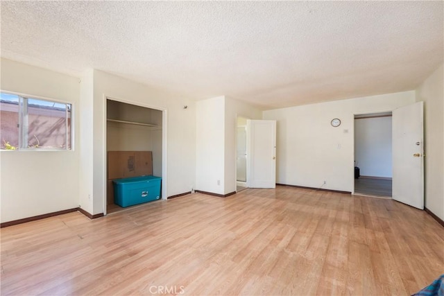unfurnished bedroom featuring a closet, light wood-style floors, a textured ceiling, and baseboards