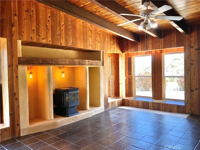 interior space with wood walls, a wood stove, wooden ceiling, dark tile patterned flooring, and ceiling fan