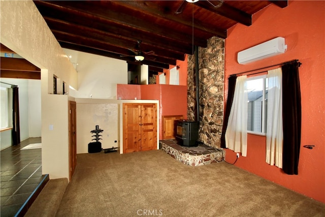 unfurnished living room featuring beamed ceiling, carpet floors, a wood stove, and an AC wall unit