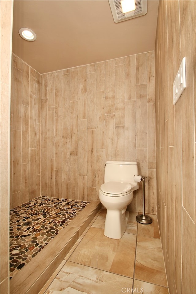 bathroom with walk in shower, toilet, and tile walls