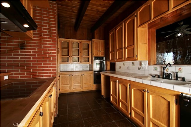 kitchen featuring backsplash, sink, black dishwasher, tile counters, and beam ceiling