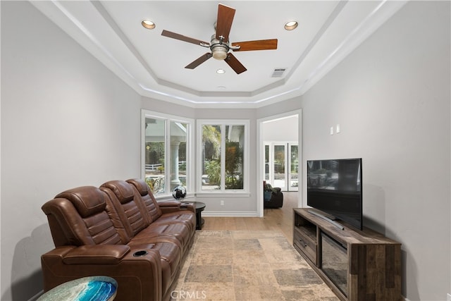 living room with a raised ceiling, light hardwood / wood-style floors, ceiling fan, and a wealth of natural light