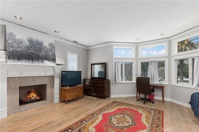 interior space featuring a tile fireplace, ornamental molding, and light wood-type flooring