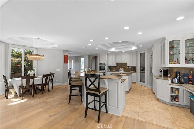 kitchen with backsplash, a raised ceiling, a wealth of natural light, and a kitchen island with sink