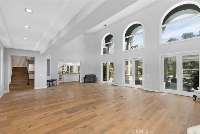 unfurnished living room featuring french doors, light wood-type flooring, and a high ceiling