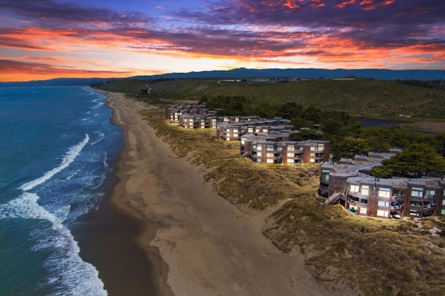 aerial view at dusk featuring a water view and a beach view