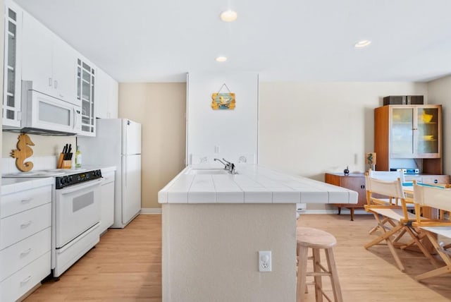 kitchen featuring tile countertops, white cabinets, a kitchen bar, and white appliances